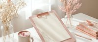 Elegant rose gold office workspace with clipboard, coffee cup, dried flowers and stationery creating a feminine productive environment for modern professionals.