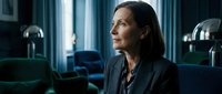 Professional middle-aged Caucasian businesswoman in dark suit sitting thoughtfully in modern office interior with elegant lighting and contemporary furniture.
