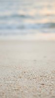 Soft sandy beach shore with gentle ocean waves and blurred seascape background, ideal for travel, vacation, and coastal lifestyle designs.