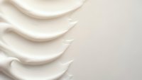 Smooth cream cosmetic texture with flowing waves creating elegant ripples on neutral background for skincare and beauty product applications.