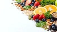 Fresh organic superfoods collection with berries, nuts, seeds, leafy greens and citrus fruits arranged on white background for healthy nutrition concepts.