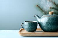 Traditional ceramic teapot and cup set in turquoise crackle glaze on wooden tray against soft blue wall, steam rising creates serene tea ceremony atmosphere.