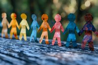 Colorful paper chain people holding hands symbolize unity, diversity, and community connection. Macro shot with soft bokeh background shows social inclusion concept.