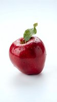 Fresh red apple with water droplets and green leaf isolated on white background for healthy eating and nutrition concepts.