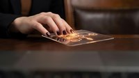 Female hand touching futuristic holographic interface with glowing digital elements on wooden desk surface for technology and innovation concepts.