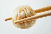 Asian steamed dumpling held by wooden chopsticks against white background, showcasing traditional Chinese dim sum cuisine in minimalist composition.