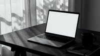 Laptop with blank white screen on dark wooden desk near window, black and white moody home office workspace with coffee mug.