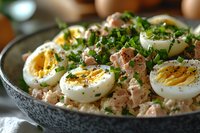 Fresh tuna salad with halved boiled eggs garnished with chopped parsley and black pepper, served in ceramic bowl. Close up view of protein-rich meal.