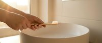 Hands stirring creamy mixture in white bowl with wooden spoon in bright kitchen. Cooking preparation, baking ingredients, culinary process for homemade recipes.