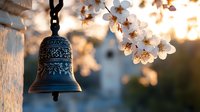 Ornate metal bell with delicate floral pattern hanging outdoors at sunset, framed by blooming white cherry blossoms creating peaceful spring atmosphere.