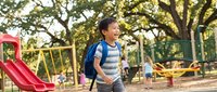 Happy young African American boy with backpack walking at school playground during sunny day, elementary student enjoying outdoor break time.