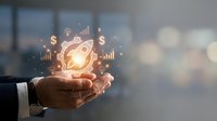Businessman hand holding glowing lightbulb with financial icons and growth charts, representing innovation, startup success, and business strategy development.