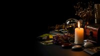 Mystical fortune telling setup with tarot cards, crystal ball, burning candle and dried herbs on dark wooden table creating atmospheric divination scene.