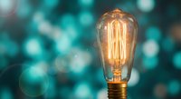 Vintage Edison bulb glowing with warm filament against turquoise bokeh background for creative lighting and innovation concepts.
