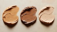 Smeared makeup foundation samples in different skin tone shades on beige background, showing texture and consistency of cosmetic product for beauty industry.