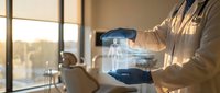 Medical professional examining transparent digital tablet displaying holographic data in modern clinic with patient consultation chair in background.