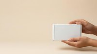 Hands holding white cardboard box on beige background for product packaging, shipping, and delivery mockup presentations.