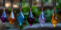 Colorful crystal pendants hanging in row against blurred natural background, featuring purple, amber, blue and pink gemstones on leather cords. Mystical jewelry display.