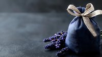 Aromatic lavender sprigs beside blue linen sachet with rustic burlap bow on dark moody background, spa wellness and aromatherapy concept.