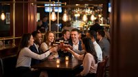 Group of diverse young professionals celebrating with drinks at upscale bar restaurant. Business colleagues toasting success in elegant venue with warm lighting.