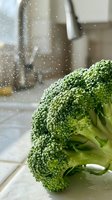 Fresh broccoli florets with water droplets in kitchen sink under running water, ideal for healthy eating, cooking, and food preparation content.