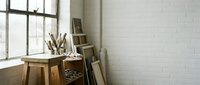 Wooden desk with pencil holder and stacked books near bright window in minimalist white brick room, suitable for office and creative workspace design projects.
