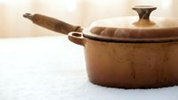 Vintage copper cooking pot with lid and wooden handle on white surface, suitable for culinary, kitchen, and home decor designs.