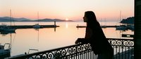 Woman silhouette gazing at serene harbor sunrise with sailboats and calm water, perfect for travel, lifestyle, and contemplation themes.