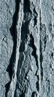 Deep cracks in weathered concrete wall surface showing natural aging and deterioration patterns with rough textured finish for construction backgrounds.