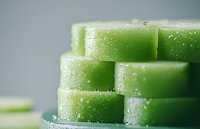 Fresh cucumber slices stacked in layers with water droplets on surface, macro photography showing crisp vegetable texture against soft gray background.