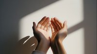 Open cupped hands in prayer or meditation gesture with dramatic sunlight and shadow creating peaceful spiritual atmosphere for wellness content.