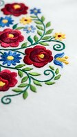 Colorful floral embroidery with red roses and blue daisies on white fabric showcasing traditional needlework craftsmanship for textile and fashion design projects.