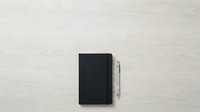 Black notebook with silver pen on light wooden surface, isolated for design use on stationery, office supplies, and business branding projects.