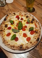 Neapolitan pizza margherita with fresh mozzarella, cherry tomatoes and basil leaves on wooden table with beer glass in restaurant setting for food photography.