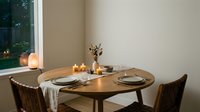 Intimate dinner setup with round wooden table, two chairs, candlelight, and table settings by window with evening view. Perfect for restaurant, hospitality, dining, and home decor concepts.