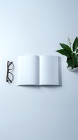 Open blank notebook with eyeglasses and green plant on clean white desk surface for workspace design and productivity concepts.