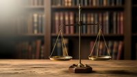 Golden brass scales of justice on wooden desk in law library with books background symbolizing legal system fairness and judicial balance.