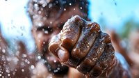 Powerful close-up of wet fist with water droplets splashing around against blurred background showing strength, determination and overcoming challenges in sports.