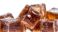 Frozen cola ice cubes with bubbles and frost, refreshing brown beverage blocks on white background, macro shot showing crystalline texture and carbonation details.