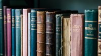 Row of vintage antique books with worn leather spines and faded titles on wooden shelf. Classic literature collection for education, library, bookstore concepts.