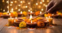 Hand lighting traditional oil lamps with marigold flowers during Diwali celebration on wooden surface with warm bokeh lights creating festive atmosphere.