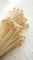 Enoki mushrooms with delicate pale stems and small rounded caps arranged in a bunch on white textured surface for culinary and food styling use.