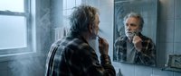 Middle-aged Caucasian man with gray beard brushing teeth in modern bathroom mirror reflection. Morning hygiene routine dental care concept.