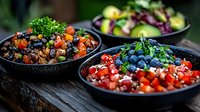 Fresh colorful vegetable and berry bowls with quinoa, tomatoes, blueberries, pomegranate seeds and herbs served on rustic wooden table, healthy eating concept.