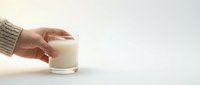Hand in cozy knit sweater holding a glass of fresh milk on white background with copy space for text.
