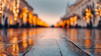 Wet cobblestone street with golden bokeh lights reflecting on rainy surface at dusk, creating atmospheric urban perspective.