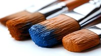 Professional art brushes with brown and blue paint on bristles against white background, macro photography showing fine detail and texture.