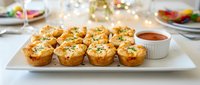 Golden baked mini quiches with herbs on white platter, perfect appetizers for brunch, party catering, holiday entertaining and elegant dining occasions.