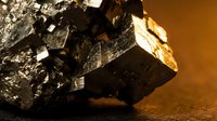 Dark metallic pyrite mineral specimen with cubic crystal formations and golden reflections on warm background for geology education and collection display.