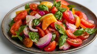 Fresh colorful tomato salad with red onions and basil leaves on rustic ceramic plate, vibrant summer dish with natural lighting and appetizing appeal.